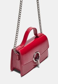 Red faux leather handbag with a structured design, a top handle, and a silver circular clasp. Features a chain shoulder strap.