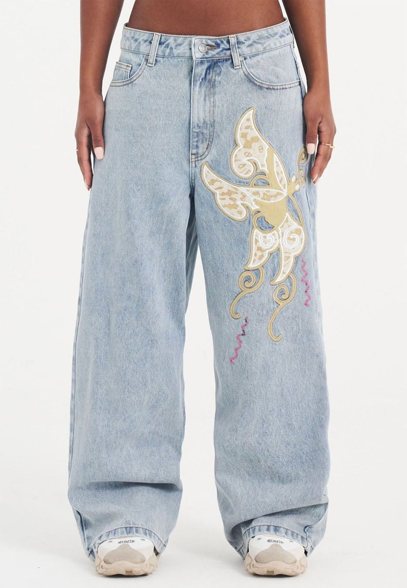Lichtblauwe wijduitbroek heeft gouden en roze vlinderborduring met spiralen, gemaakt van denim met een zachte, versleten textuur.