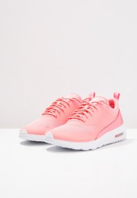 Rosa sportskor med mesh-överdel, rund tå och vit sula. Har en dragöglan vid hälen och Nike-logotyp på sidan.