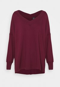 Burgundy långärmad topp med bred V-urringning, sänkta axlar, sidslitsar och ribbad mudd. Mjuk, texturerad tyg för bekväm användning.