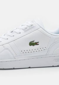 Hvit lær sneakers med en grønn krokodille-logo, rund tå, flate lisser og perforerte detaljer på sidene. Gummi såle.