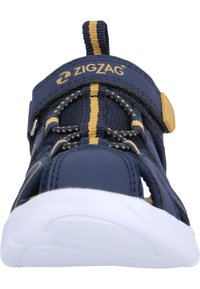 Laivastonsiniset sandaalit, joissa on verkkomateriaali yläosa, joustavat nauhat ja tarranauha. Valkoinen kumipohja, jossa on aukkoja hengittävyyden lisäämiseksi. Siksak-logo on esillä.