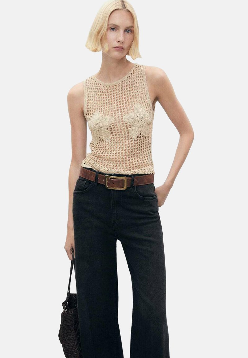 Beige knitted tank top with floral crochet details, paired with high-waisted black wide-leg jeans and a brown belt, holding a black bag.