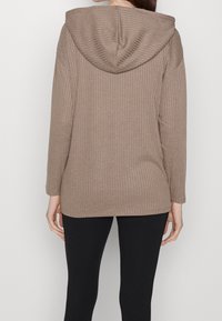 Felpa con cappuccio marrone a coste, dal texture morbido, maniche lunghe e orlo leggermente curvo. Presenta un cappuccio foderato e una vestibilità rilassata.