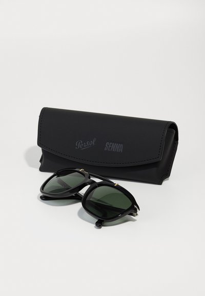 Juodos Persol saulės akinių modelis su žaliais objektyvais, kvadratinio dizaino ir auksinėmis detalėmis, kartu su atitinkamu juodu odiniu dėklu.