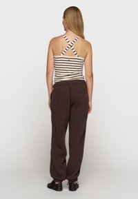 Stribet tanktop med krydsede stropper, parret med mørkebrune sweatpants med elastisk talje og manchetter. Sorte sko fuldender outfittet.
