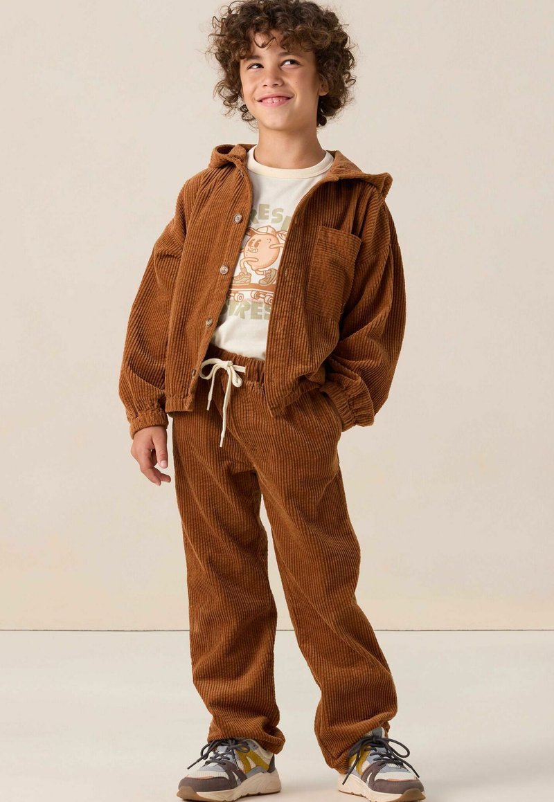 Ensemble en velours côtelé marron composé d'une veste et d'un pantalon, avec un T-shirt graphique blanc en dessous. Comprend une capuche, des boutons et une taille élastique avec cordon de serrage. Tissu texturé.