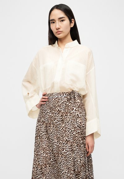 Μπεζ, ελαφριά μπλούζα με κάθετες ρίγες, γιακά με κουμπιά και μανσέτες, συνδυασμένη με μακριά καφέ φούστα με λεοπάρ μοτίβο και ζωνάκι στη μέση.