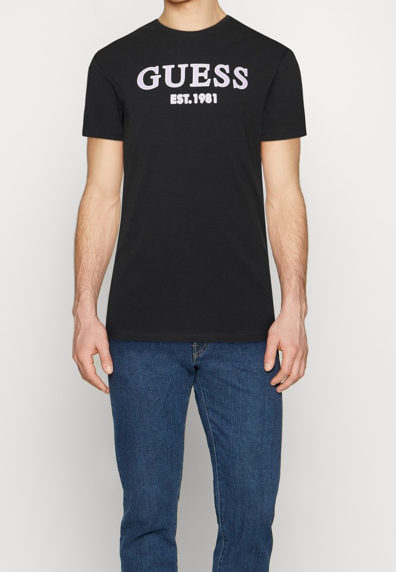 Sort bomuld t-shirt med "GUESS" i fed, pink skrifttype og "EST. 1981" nedenunder. Rund halsudskæring med korte ærmer.