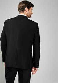 Zwarte colbert met een getailleerde pasvorm, pieklapels en een sluiting met drie knopen. Vlotte textuur, minimale naden en lange mouwen.