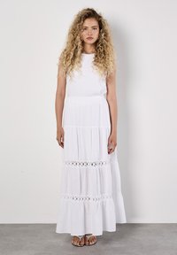 Abito maxi bianco senza maniche realizzato in tessuto leggero, caratterizzato da un design a strati, dettagli a occhio di pernice sull'orlo e una silhouette rilassata.