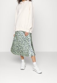 Sudadera rosa clara con cordones, combinada con una falda midi floral verde con acentos azules y morados; llevada con zapatillas blancas.