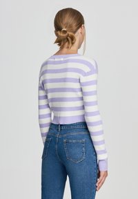 Maglione accorciato con righe orizzontali viola e bianche, texture a coste e maniche lunghe. Abbinato a jeans aderenti blu con due tasche posteriori.