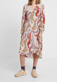 Robe portefeuille à manches longues, arborant un motif abstrait multicolore dans des tons d'orange, de violet et de beige, faite de tissu léger.
