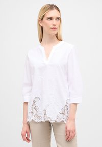 Hvid bomuldsbluse med trekvartærmer, med blomsterbroderi og blondekant foran, V-hals design.