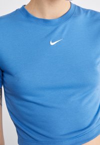 Blå bomullstopp med rund hals och korta ärmar. Har en vit Nike-logotyp centralt på bröstet. Slät textur.