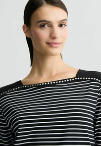 Zwart-wit gestreepte top met een brede halslijn versierd met metallic studs langs de schoudernaad. Zachte stoftextuur.