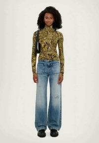 Langermet gul og svart mønstrete topp kombinert med lyseblå vide jeans, båret med svarte plattform sko og en svart skulderveske.