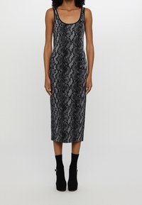 Femme portant une robe midi sans manches à motif python noir et gris avec des bottines noires, sur un fond gris uni.