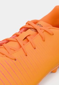 Spilgti oranžs futbola apavi ar gludu tekstūru, ar rozā horizontālām svītrām un oranžām auklām. Iekļauta maza melna logotipa detaļa.