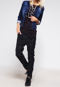 Jeansjacka i mörkblått med en figurnära design och kontrastärmar, tillsammans med en svart t-shirt med vit text. Svarta byxor och sneakers.