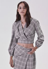 Top a quadri tagliato con maniche lunghe e puff in bianco e nero, abbinato a una gonna coordinata, caratterizzata da una superficie liscia e un design aderente.