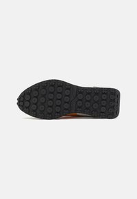 Talpa de sneaker din cauciuc negru cu modele circulare de tracțiune. Partea laterală atașată prezintă un material textil gri și portocaliu. Design durable și flexibil pentru tracțiune.
