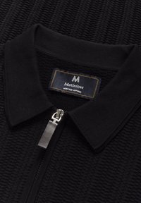 Black knit pullover with a ribbed texture, featuring a zip closure and a polo collar. Label reads "Matinique Heritage Apparel."