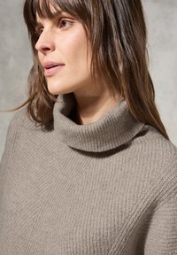 Beige gestrickter Pullover mit hohem, geripptem Rollkragen und strukturiertem Muster, ausgestattet mit langen Ärmeln und einer lockeren Passform.