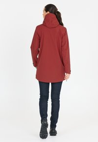 Röd vattentät jacka med huva, långa ärmar och rundad nederkant. Matchad med mörkblå jeans och svarta robusta skor.