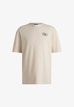 T-shirt beige à manches courtes en tissu doux, avec un col rond et un petit logo noir brodé sur la poitrine gauche.