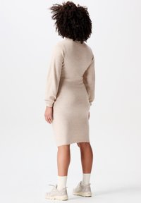 Beige gebreid jurk met lange mouwen, aansluitende pasvorm en knielange snit. Draag het met lichte sneakers en witte geribde sokken.