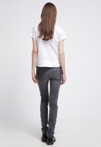 Vitt kortärmat linne, grå slim-fit jeans och svarta skor. Släta tyger och enkel design. Inga synliga mönster eller grafik.