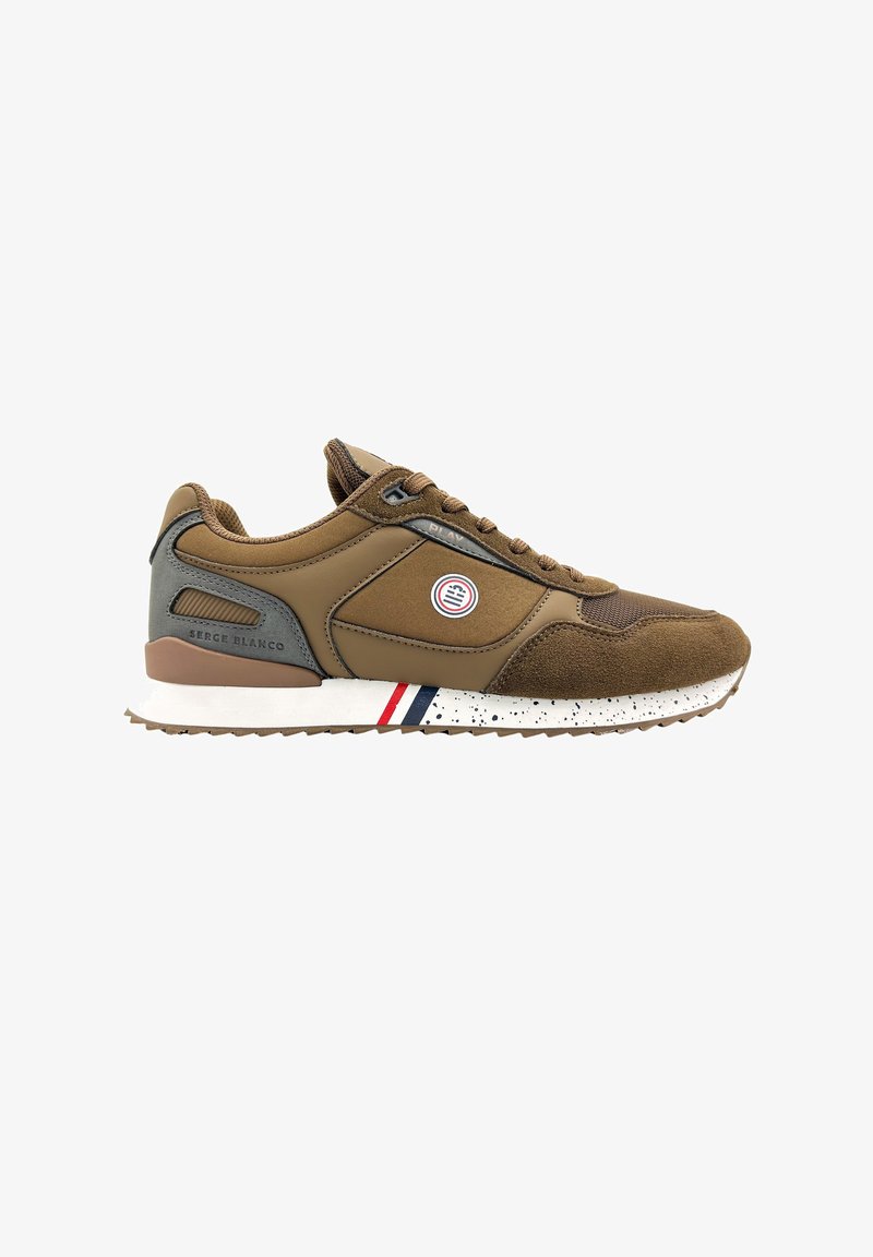 Zapatilla deportiva marrón con materiales de ante y sintéticos, presenta un logo redondo, suela blanca con motas y rayas decorativas rojas y azules.