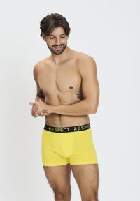 Boxer briefs in cotone giallo con un elastico nero in vita etichettato "RISPETTO". Il design presenta una forma aderente e una consistenza liscia.