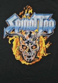 Černé tričko s grafikou lebky s rohy obklopené plameny. Text "Spinal Tap" ve stylizované modré barvě nad obrázkem.