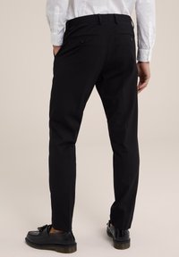 Svarta skräddarsydda byxor med slim fit, med bakfickor och en mjuk yta. Bärs med svarta skor och en vit långärmad skjorta.