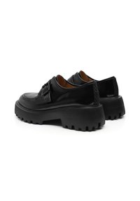 Zapatos de charol negro con una suela gruesa y texturizada. Presentan un detalle trenzado en el talón y un sutil acento de hebilla en la parte superior.