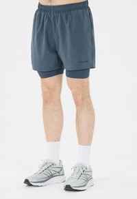 Korte sportieve shorts van donkergrijze stof met een elastische tailleband, gelaagd over nauwsluitende binnenbroeken. Grijze hardloopschoenen met zwarte accenten.