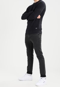 Marinblå ribbad stickad tröja, svarta jeans och vita sneakers. Tröjan har rundad halsringning och en strukturerad mönster. De svarta jeansen har en slim fit.