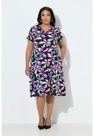 Kvinde iført knælange sort kjole med flerfarvet abstrakt blomsterprint, korte ærmer og v-hals, kombineret med sorte hæle.