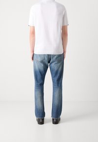 T-shirt blanc à manches courtes et jean en denim bleu clair, avec une coupe droite et un léger délavage. Des chaussures noires complètent la tenue.