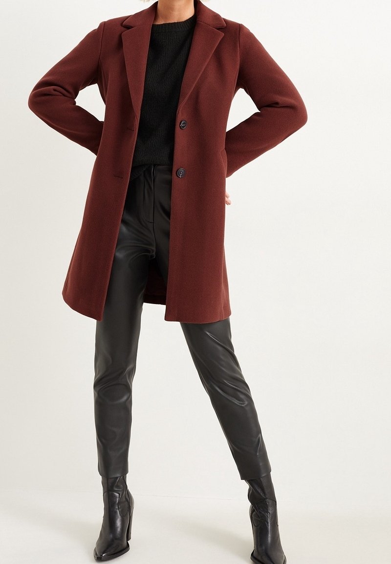 Viininpunainen takki räätälöidyllä leikkauksella, pitkät hihat ja kaksi nappia; yhdistetty mustiin tekonahkahousuihin ja nilkkureihin.