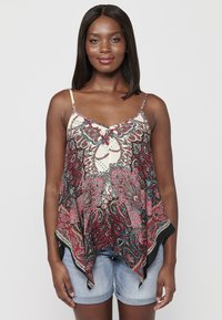 Top sans manches multicolore avec un motif paisley rouge, bleu et crème. Design fluide avec un ourlet asymétrique ; associé à des shorts en denim.