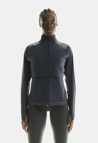 Veste de sport marine avec fermeture éclair devant, manches longues, et un design ajusté avec des panneaux latéraux contrastés et une texture lisse.