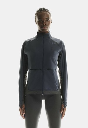 Veste de sport marine avec fermeture éclair devant, manches longues, et un design ajusté avec des panneaux latéraux contrastés et une texture lisse.