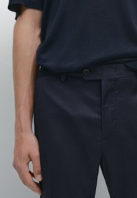 Navy blue trousers with a subtle pinstripe pattern, featuring a button closure and a tapered design. Soft fabric texture and sleek silhouette.