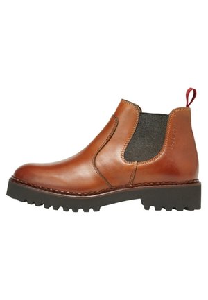 Bota Chelsea de cuero marrón con panel lateral elástico negro, tira roja de sujeción en el talón, suela gruesa de tacos negra y costuras visibles alrededor de la suela.