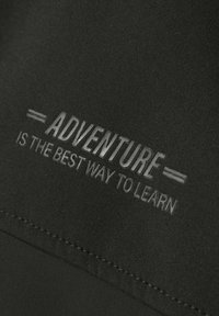 Schwarzer Stoff mit geprägtem Text "ABENTEUER IST DER BESTE WEG ZU LERNEN" und dezenten Nähdetails. Glatte, matte Textur.