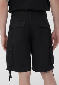 Pantaloni cargo neri realizzati in un tessuto resistente, con due ampie tasche laterali, cordini regolabili all'orlo e una tasca posteriore con cerniera.